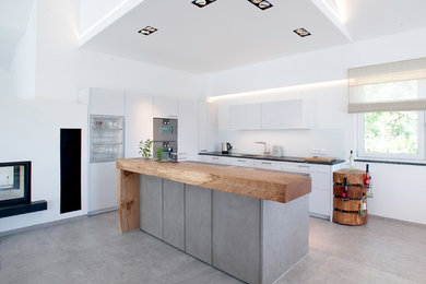 Design ideas for a modern kitchen in Munich with a single-bowl sink, flat-panel cabinets, white cabinets, stainless steel appliances, concrete floors, with island, grey floor and black benchtop.