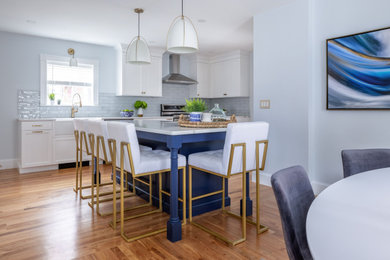 Inspiration for a transitional medium tone wood floor and brown floor eat-in kitchen remodel in Boston with a farmhouse sink, shaker cabinets, white cabinets, quartz countertops, blue backsplash, glass tile backsplash, stainless steel appliances, an island and white countertops