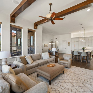 Open-concept living room and kitchen with dark wood ceiling beams and arched win