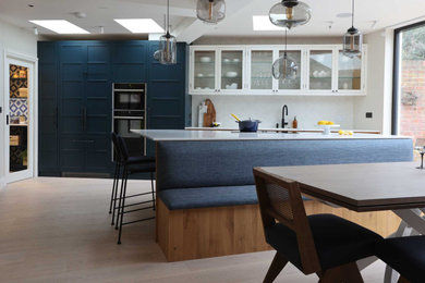 This is an example of a large single-wall open plan kitchen in London with an integrated sink, shaker cabinets, blue cabinets, quartz worktops, white splashback, cement tile splashback, stainless steel appliances, light hardwood flooring, an island and white worktops.
