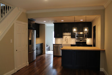 Example of a mid-sized eclectic medium tone wood floor eat-in kitchen design in Philadelphia with a farmhouse sink, beaded inset cabinets, dark wood cabinets, granite countertops, white backsplash, subway tile backsplash, stainless steel appliances and a peninsula
