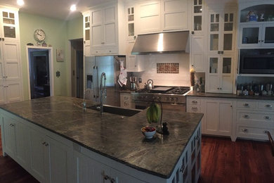 Eat-in kitchen - large traditional galley medium tone wood floor and brown floor eat-in kitchen idea in Philadelphia with a farmhouse sink, recessed-panel cabinets, white cabinets, granite countertops, white backsplash, ceramic backsplash, stainless steel appliances and an island