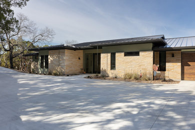 Example of a transitional green one-story stone house exterior design in Austin with a butterfly roof, a metal roof and a black roof