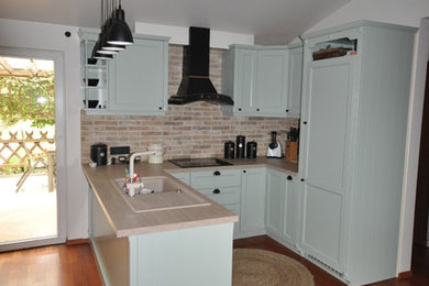 Example of a tuscan medium tone wood floor and red floor kitchen design in Other with a single-bowl sink, green cabinets, laminate countertops, beige backsplash, brick backsplash, black appliances and beige countertops