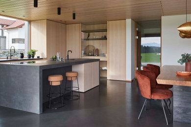 Offene Moderne Küche mit flächenbündigen Schrankfronten, hellen Holzschränken, Betonarbeitsplatte, Kücheninsel, schwarzem Boden und schwarzer Arbeitsplatte in München
