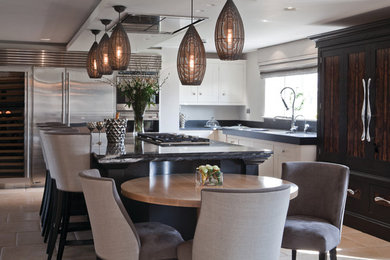 This is an example of a medium sized country l-shaped kitchen/diner with shaker cabinets, white cabinets, granite worktops, grey splashback, stone slab splashback, stainless steel appliances, limestone flooring and multiple islands.