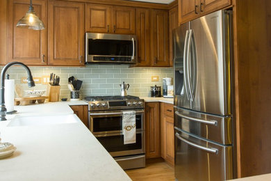Mid-sized country u-shaped medium tone wood floor and brown floor enclosed kitchen photo in Chicago with an island, a farmhouse sink, raised-panel cabinets, medium tone wood cabinets, quartz countertops, green backsplash, subway tile backsplash and stainless steel appliances