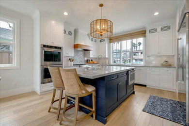 Mid-sized beach style l-shaped vinyl floor and beige floor eat-in kitchen photo in San Francisco with a farmhouse sink, beaded inset cabinets, white cabinets, quartzite countertops, white backsplash, ceramic backsplash, stainless steel appliances, an island and gray countertops