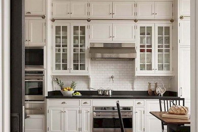 Large elegant l-shaped dark wood floor and brown floor eat-in kitchen photo in Columbus with a farmhouse sink, recessed-panel cabinets, white cabinets, granite countertops, white backsplash, ceramic backsplash, stainless steel appliances and black countertops