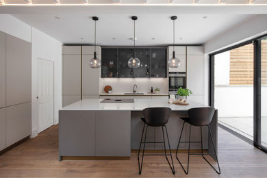 Medium sized modern l-shaped kitchen/diner in London with a submerged sink, flat-panel cabinets, grey cabinets, quartz worktops, black appliances, dark hardwood flooring, an island, brown floors and white worktops.