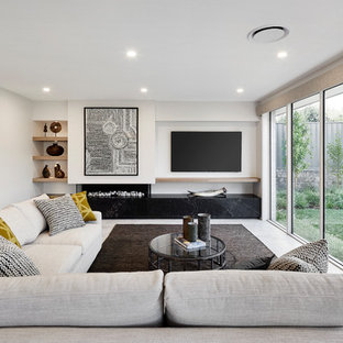 Modern inredning av ett allrum med öppen planlösning, med vita väggar, en bred öppen spis, en spiselkrans i gips, en väggmonterad TV och vitt golv