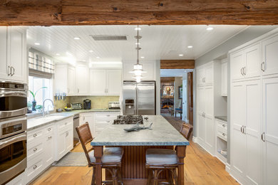 Large beach style eat-in kitchen in Orange County with beaded inset cabinets, white cabinets, marble benchtops, stainless steel appliances, light hardwood floors, with island, brown floor and grey benchtop.