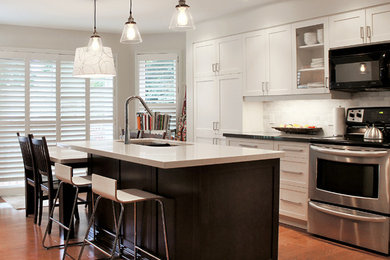 Mid-sized transitional l-shaped medium tone wood floor open concept kitchen photo in Toronto with an undermount sink, recessed-panel cabinets, white cabinets, quartz countertops, stone tile backsplash, stainless steel appliances, an island and beige backsplash