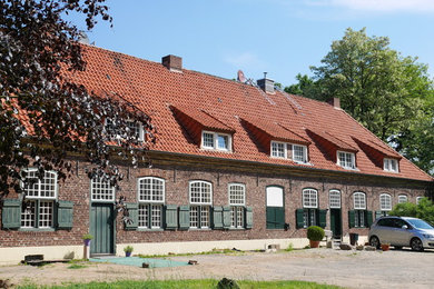 Aménagement d'une grande façade de maison rouge campagne en brique à un étage avec un toit à deux pans et un toit en tuile.