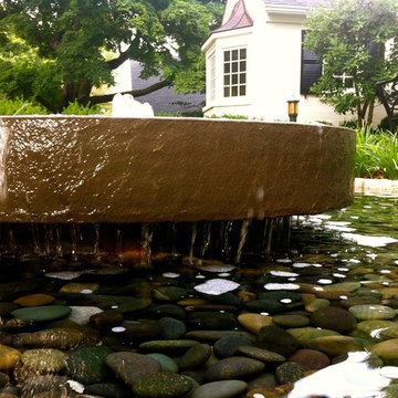 Polished bluestone millstone water feature with pebbles below.