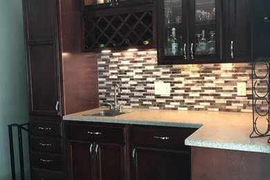 Mid-sized transitional l-shaped vinyl floor and black floor enclosed kitchen photo in Chicago with a drop-in sink, recessed-panel cabinets, dark wood cabinets, solid surface countertops, gray backsplash, mosaic tile backsplash and stainless steel appliances