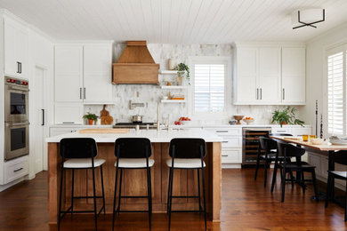 Photo of a country l-shaped open plan kitchen in Los Angeles with a farmhouse sink, shaker cabinets, white cabinets, quartz benchtops, multi-coloured splashback, marble splashback, stainless steel appliances, medium hardwood floors, with island, brown floor, white benchtop and timber.