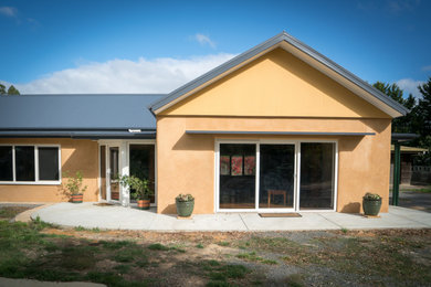 Foto della villa grande arancione country a un piano con rivestimento in stucco, copertura in metallo o lamiera e tetto blu
