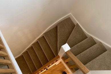 Inspiration for a mid-sized contemporary carpeted curved staircase in Manchester with carpet risers and wood railing.