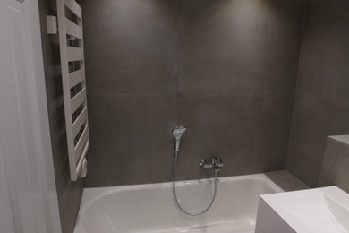 Mittelgroßes Modernes Badezimmer mit flächenbündigen Schrankfronten, weißen Schränken, Badewanne in Nische, Wandtoilette, grauen Fliesen, weißer Wandfarbe, integriertem Waschbecken, Mineralwerkstoff-Waschtisch, grauem Boden, weißer Waschtischplatte, Steinfliesen, Einzelwaschbecken und schwebendem Waschtisch in München