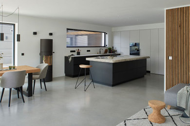 Mittelgroße Moderne Küche mit flächenbündigen Schrankfronten, weißen Schränken, schwarzen Elektrogeräten, Betonboden, Kücheninsel, grauem Boden und weißer Arbeitsplatte in München