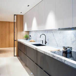Diseño de cocina larga, barra de cocina y gris y negra, minimalista, de tamaño medio, abierta, sin isla, con fregadero bajoencimera, armarios con paneles lisos, puertas de armario grises, encimera de mármol, salpicadero blanco, salpicadero de mármol, electrodomésticos negros, suelo beige y encimeras blancas