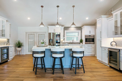 Example of a large minimalist galley brown floor and medium tone wood floor eat-in kitchen design in Tampa with shaker cabinets, white cabinets, gray backsplash, subway tile backsplash, stainless steel appliances and an island