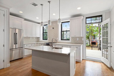 Open concept kitchen - mid-sized transitional l-shaped medium tone wood floor and brown floor open concept kitchen idea in New York with an undermount sink, shaker cabinets, white cabinets, quartz countertops, beige backsplash, subway tile backsplash, stainless steel appliances and an island