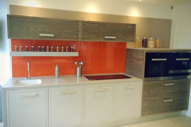 Small modern single-wall kitchen in London with an integrated sink, flat-panel cabinets, light wood cabinets, solid surface benchtops, orange splashback, glass sheet splashback, stainless steel appliances and no island.