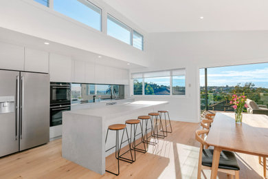 Design ideas for a large beach style galley open plan kitchen in Sydney with a double-bowl sink, flat-panel cabinets, grey cabinets, solid surface benchtops, mirror splashback, stainless steel appliances, laminate floors, with island, beige floor and grey benchtop.