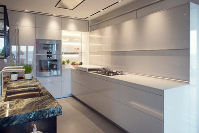 Mittelgroße Moderne Wohnküche in L-Form mit Glas-Arbeitsplatte, flächenbündigen Schrankfronten, weißen Schränken, Küchengeräten aus Edelstahl, Betonboden, Kücheninsel und grauem Boden in Frankfurt am Main