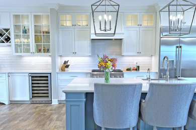 This is an example of an expansive traditional l-shaped kitchen pantry with a submerged sink, recessed-panel cabinets, blue cabinets, engineered stone countertops, white splashback, metro tiled splashback, stainless steel appliances, vinyl flooring, an island, brown floors and white worktops.