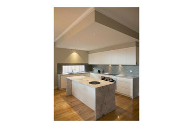 This is an example of a modern eat-in kitchen in Melbourne with a double-bowl sink, flat-panel cabinets, white cabinets, marble benchtops, metallic splashback, glass sheet splashback, stainless steel appliances, light hardwood floors and with island.