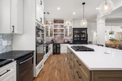 Inspiration for a large transitional medium tone wood floor eat-in kitchen remodel in Dallas with an undermount sink, glass-front cabinets, white cabinets, quartz countertops, brick backsplash, black appliances, an island and black countertops