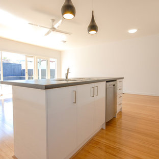 Zweizeilige, Mittelgroße Moderne Küche mit Vorratsschrank, Doppelwaschbecken, flächenbündigen Schrankfronten, weißen Schränken, Onyx-Arbeitsplatte, Küchenrückwand in Weiß, Rückwand aus Glasfliesen, Küchengeräten aus Edelstahl, hellem Holzboden, Kücheninsel, braunem Boden und schwarzer Arbeitsplatte in Melbourne