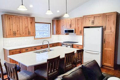 Open concept kitchen - mid-sized rustic l-shaped vinyl floor, brown floor and vaulted ceiling open concept kitchen idea in Other with an undermount sink, flat-panel cabinets, medium tone wood cabinets, quartz countertops, white backsplash, ceramic backsplash, stainless steel appliances, an island and white countertops