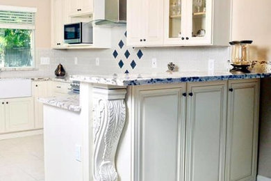 Inspiration for a mid-sized transitional u-shaped porcelain tile and white floor eat-in kitchen remodel in Other with a farmhouse sink, raised-panel cabinets, white cabinets, tile countertops, white backsplash, porcelain backsplash, black appliances, a peninsula and black countertops