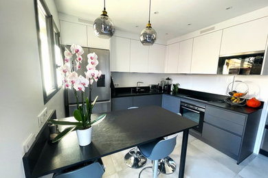 Réalisation d'une cuisine encastrable, bicolore et grise et blanche minimaliste en U fermée et de taille moyenne avec un évier encastré, un placard à porte affleurante, des portes de placard blanches, un plan de travail en granite, une crédence noire, une crédence en granite, un sol en carrelage de céramique, îlot, un sol gris et plan de travail noir.
