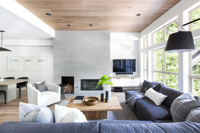 Inspiration for a large contemporary open concept living room in Vancouver with white walls, light hardwood floors, a standard fireplace, a concrete fireplace surround, a wall-mounted tv and brown floor.