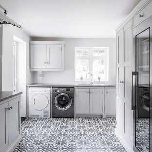ケントの巨大なコンテンポラリースタイルのおしゃれな家事室 (シングルシンク、シェーカースタイル扉のキャビネット、グレーのキャビネット、ラミネートカウンター、グレーの壁、セラミックタイルの床、左右配置の洗濯機・乾燥機、黄色い床、グレーのキッチンカウンター) の写真