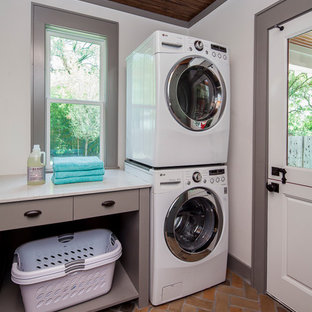 オースティンの中サイズのおしゃれなランドリールーム (シェーカースタイル扉のキャビネット、茶色いキャビネット、クオーツストーンカウンター、白い壁、レンガの床、上下配置の洗濯機・乾燥機、オレンジの床) の写真