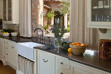 This is an example of an expansive mediterranean l-shaped eat-in kitchen in Phoenix with glass-front cabinets, a farmhouse sink, white cabinets, solid surface benchtops, white splashback, subway tile splashback, stainless steel appliances, medium hardwood floors, with island and brown floor.