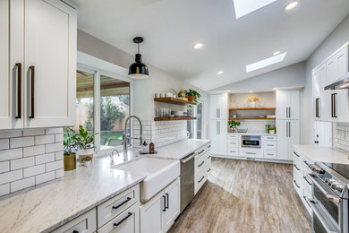This is an example of a mid-sized transitional galley kitchen pantry in Seattle with a farmhouse sink, shaker cabinets, marble benchtops, white splashback, subway tile splashback, stainless steel appliances, laminate floors, no island, brown floor and white benchtop.