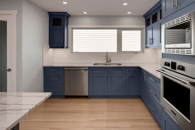 Example of a transitional l-shaped light wood floor kitchen design in Calgary with an undermount sink, shaker cabinets, gray cabinets, quartzite countertops, white backsplash, cement tile backsplash, stainless steel appliances and white countertops