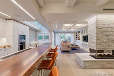 Example of a large trendy open concept light wood floor, brown floor and coffered ceiling family room design in San Francisco with white walls, a two-sided fireplace, a stone fireplace and a media wall