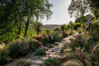 This is an example of a large mediterranean back garden in Wiltshire with a garden path and natural stone paving.