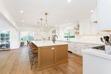 Large elegant u-shaped medium tone wood floor and brown floor open concept kitchen photo in Dallas with an undermount sink, shaker cabinets, white cabinets, quartz countertops, white backsplash, marble backsplash, white appliances, an island and white countertops