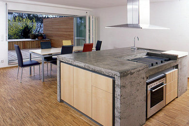 Photo of a large contemporary eat-in kitchen in Nuremberg with with island, flat-panel cabinets, light wood cabinets, concrete benchtops, stainless steel appliances, an undermount sink and light hardwood floors.