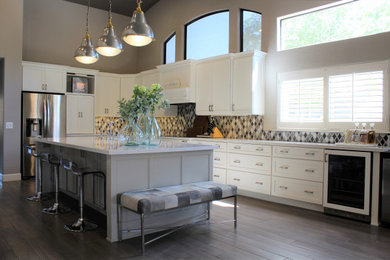 Inspiration for a large transitional l-shaped porcelain tile and gray floor kitchen remodel in Phoenix with a farmhouse sink, shaker cabinets, white cabinets, quartz countertops, metallic backsplash, metal backsplash, stainless steel appliances, an island and white countertops