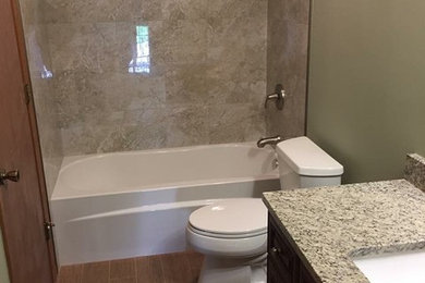 This is an example of a mid-sized transitional master bathroom in Chicago with raised-panel cabinets, dark wood cabinets, an alcove tub, a shower/bathtub combo, a two-piece toilet, beige tile, porcelain tile, green walls, porcelain floors, an undermount sink, granite benchtops, brown floor and a shower curtain.
